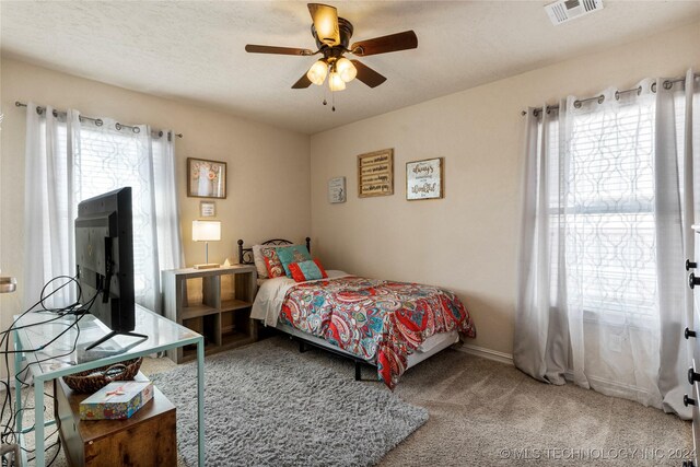 carpeted bedroom featuring ceiling fan, a textured ceiling, visible vents, and baseboards