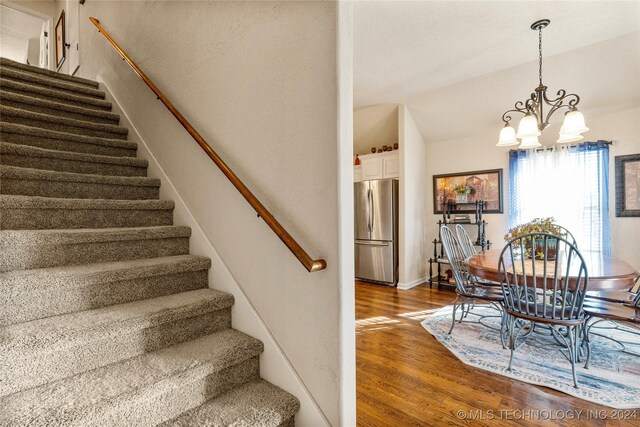 stairs featuring lofted ceiling, a notable chandelier, and wood finished floors