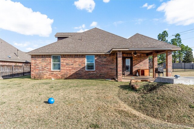 rear view of property with ceiling fan, fence, a lawn, and brick siding