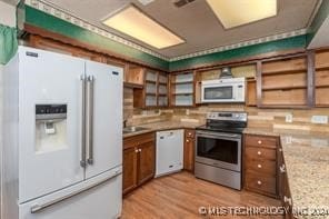 kitchen with backsplash, light stone counters, light hardwood / wood-style floors, and white appliances