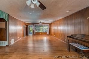 living room featuring wood-type flooring, ceiling fan, and wood walls