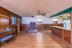 interior space with ceiling fan, light hardwood / wood-style floors, a textured ceiling, and wooden walls