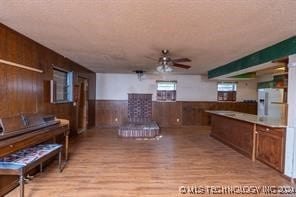 kitchen featuring a textured ceiling, ceiling fan, wooden walls, white refrigerator, and light hardwood / wood-style floors