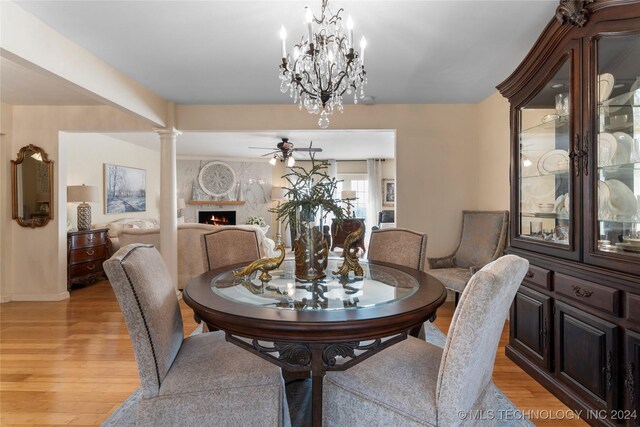 dining room featuring light hardwood / wood-style floors, ceiling fan, decorative columns, and a fireplace