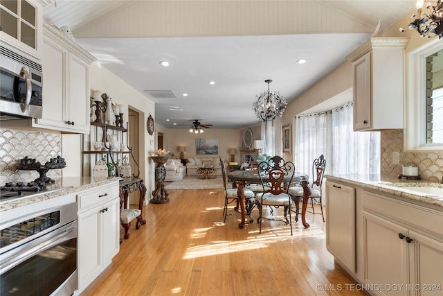 kitchen with stainless steel appliances, light hardwood / wood-style flooring, decorative light fixtures, backsplash, and ceiling fan with notable chandelier