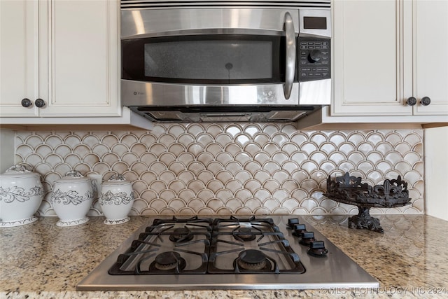 kitchen featuring white cabinets, gas stovetop, light stone counters, and tasteful backsplash