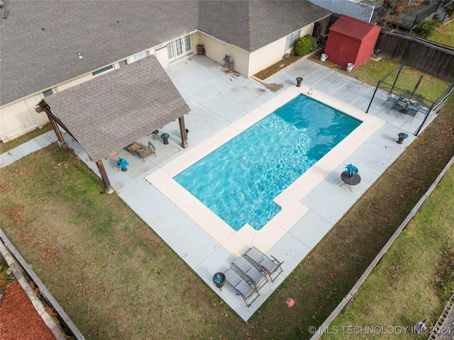 view of pool featuring a lawn, a patio, and a storage unit