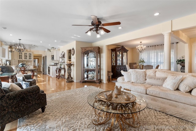 living room featuring ceiling fan with notable chandelier, decorative columns, and light hardwood / wood-style floors