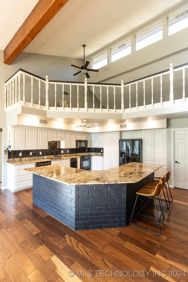 kitchen with black appliances, white cabinetry, a spacious island, and a towering ceiling