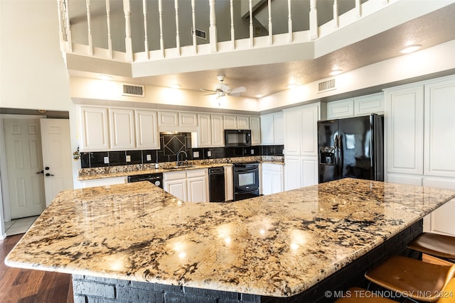 kitchen with black appliances, wood-type flooring, ceiling fan, light stone counters, and white cabinetry