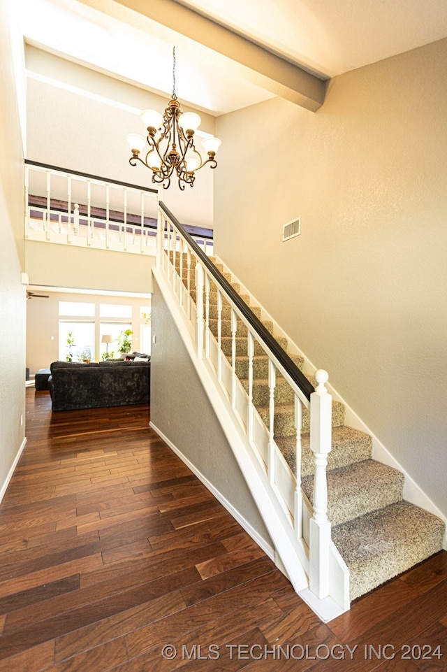 stairway featuring beamed ceiling, hardwood / wood-style flooring, and an inviting chandelier