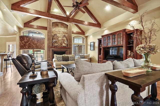 living room with plenty of natural light, beam ceiling, light wood-type flooring, and high vaulted ceiling