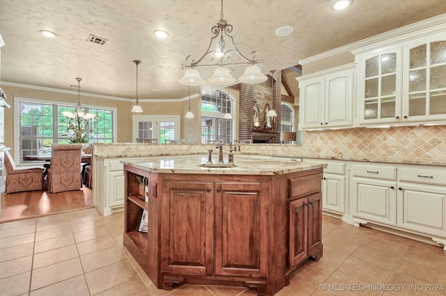 kitchen featuring sink, light stone counters, crown molding, decorative light fixtures, and a center island with sink