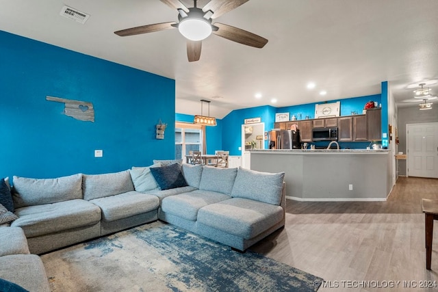 living room featuring ceiling fan with notable chandelier and light hardwood / wood-style flooring