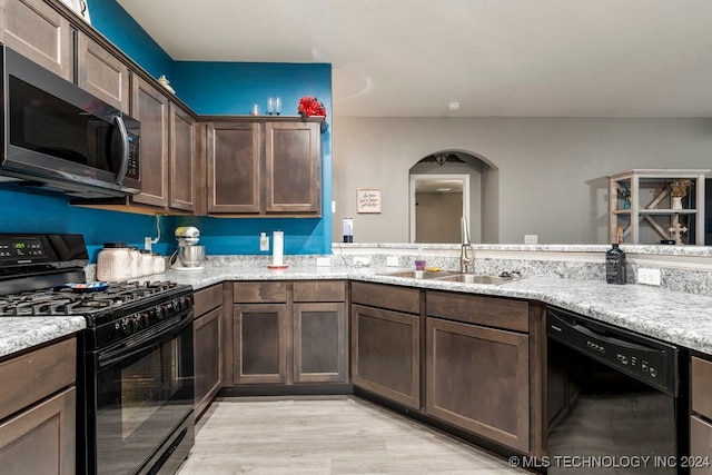 kitchen featuring light stone countertops, dark brown cabinets, sink, black appliances, and light hardwood / wood-style flooring