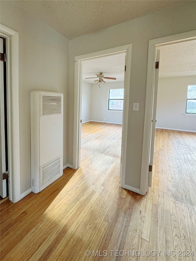 hall featuring a healthy amount of sunlight, a textured ceiling, and light hardwood / wood-style floors