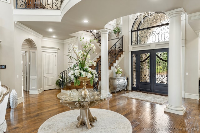 entrance foyer with french doors, dark hardwood / wood-style flooring, decorative columns, a towering ceiling, and ornamental molding