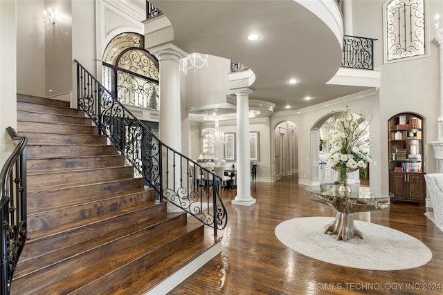 interior space featuring ornate columns, ornamental molding, a towering ceiling, a notable chandelier, and dark hardwood / wood-style flooring