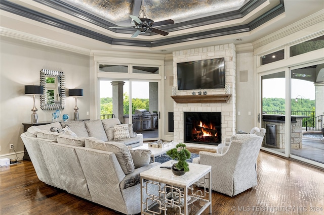 living room featuring dark hardwood / wood-style floors, ceiling fan, ornamental molding, a fireplace, and a tray ceiling