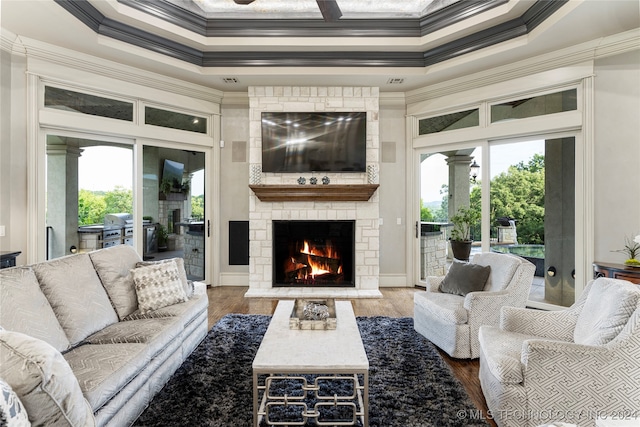 living room with a wealth of natural light, crown molding, hardwood / wood-style floors, and a stone fireplace