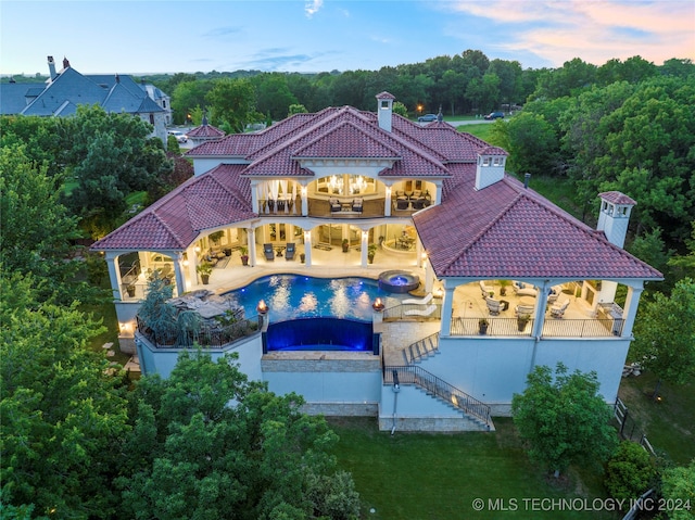 back house at dusk with a pool with hot tub, a patio area, and a balcony