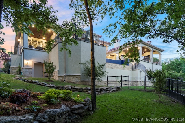 property exterior at dusk with a balcony and a yard