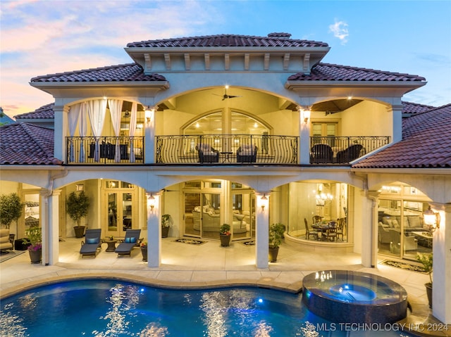 back house at dusk featuring a patio area, a balcony, and a pool with hot tub