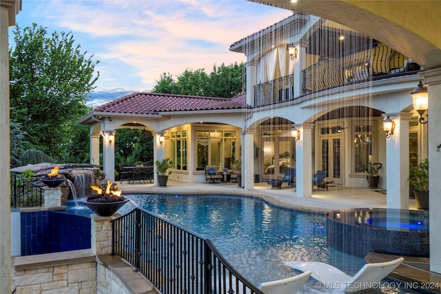 pool at dusk with an outdoor fire pit, an in ground hot tub, and a patio