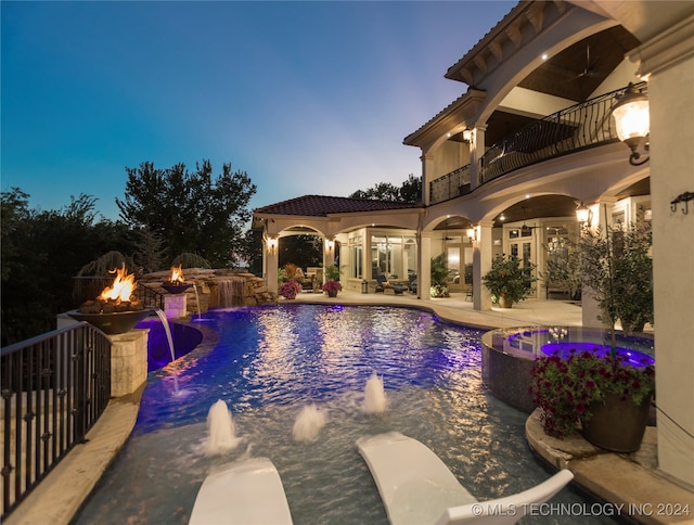 pool at dusk with a fire pit, pool water feature, ceiling fan, an in ground hot tub, and a patio area