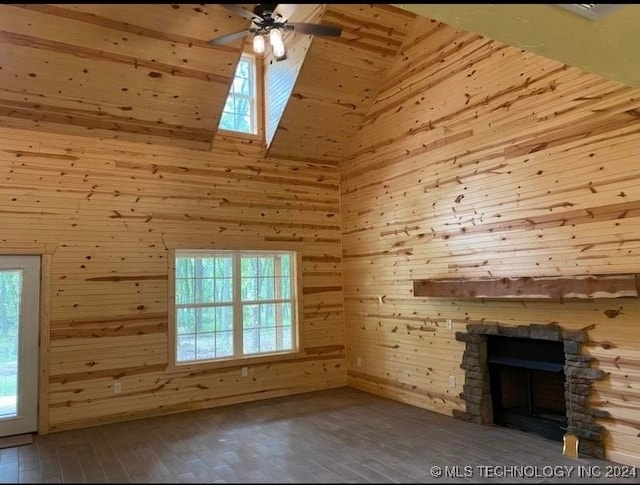 unfurnished living room with a stone fireplace, a wealth of natural light, and wooden walls