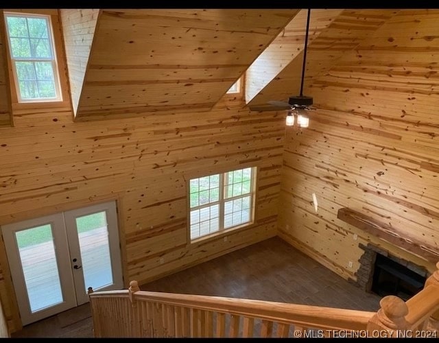 bonus room with ceiling fan, french doors, a stone fireplace, wood walls, and hardwood / wood-style floors