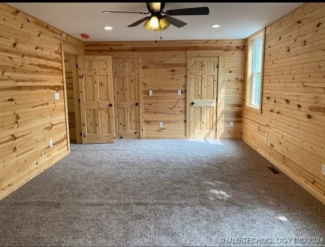 carpeted empty room featuring wood walls and ceiling fan