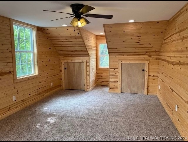 additional living space with carpet flooring, wood walls, and ceiling fan