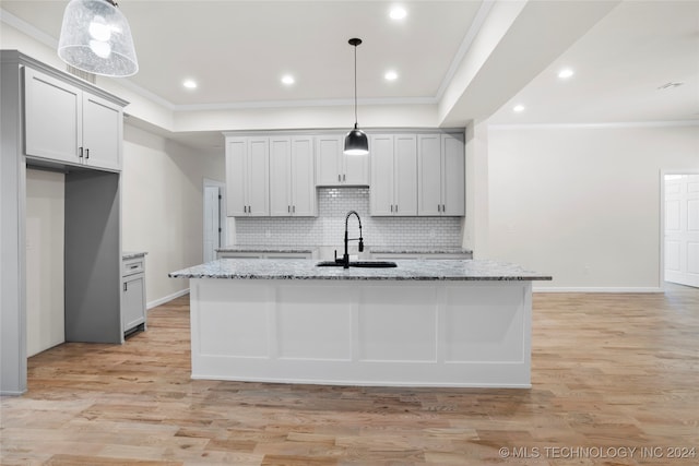 kitchen with light stone countertops, hanging light fixtures, a kitchen island with sink, and sink