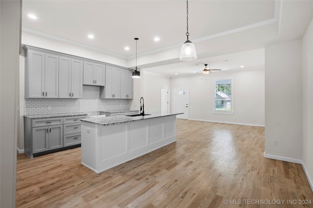 kitchen featuring ceiling fan, sink, an island with sink, pendant lighting, and light hardwood / wood-style floors