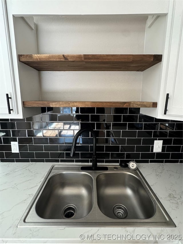 interior details with white cabinetry, sink, backsplash, and light stone countertops