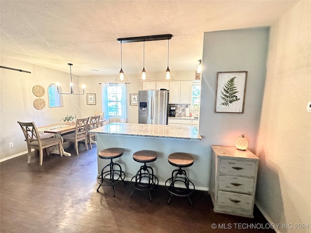 kitchen with hanging light fixtures, light stone counters, stainless steel refrigerator with ice dispenser, a breakfast bar, and white cabinets