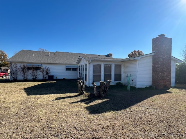 rear view of property featuring central air condition unit and a lawn