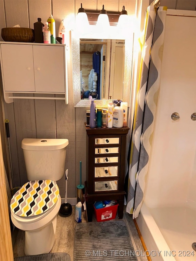 bathroom with hardwood / wood-style flooring, shower / bath combination with curtain, and toilet