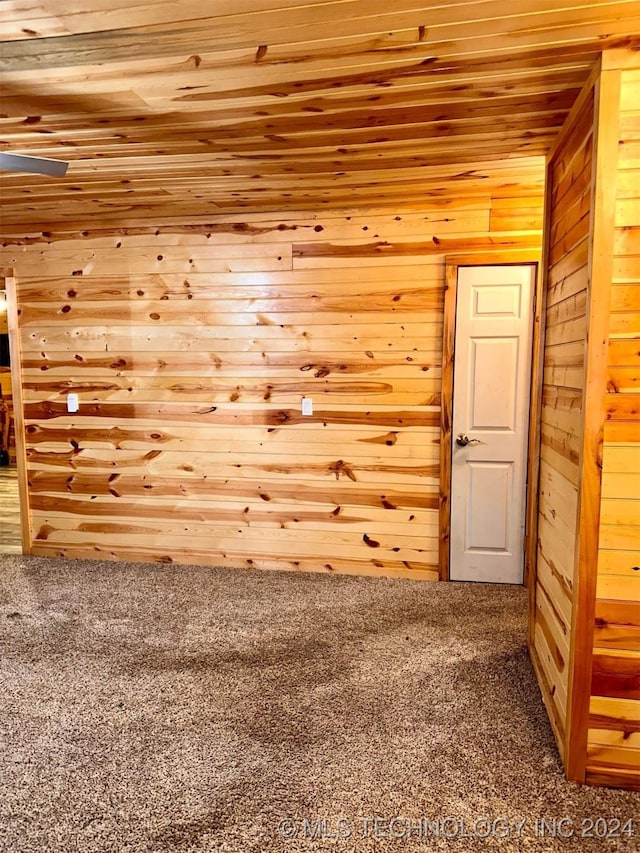 carpeted spare room with wood walls and wooden ceiling