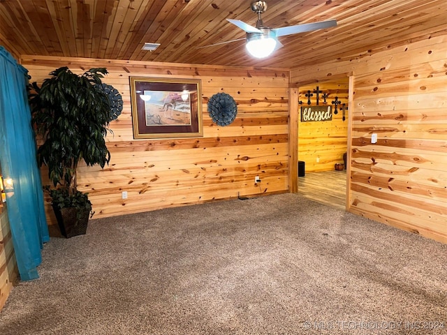 carpeted empty room with ceiling fan, wood ceiling, and wood walls