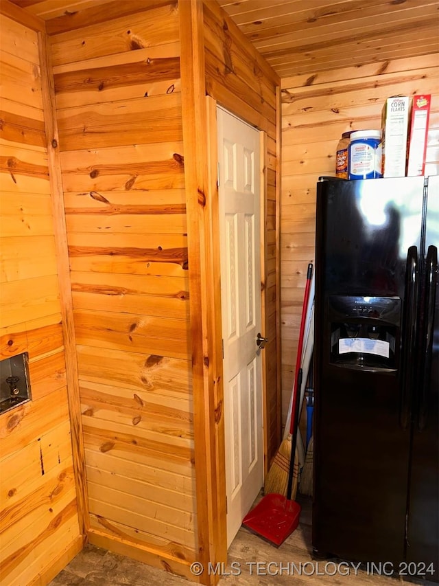 interior space with black refrigerator with ice dispenser and wooden walls