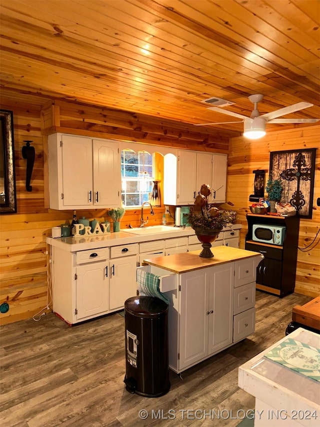 kitchen with wooden walls, a center island, white cabinets, and ceiling fan