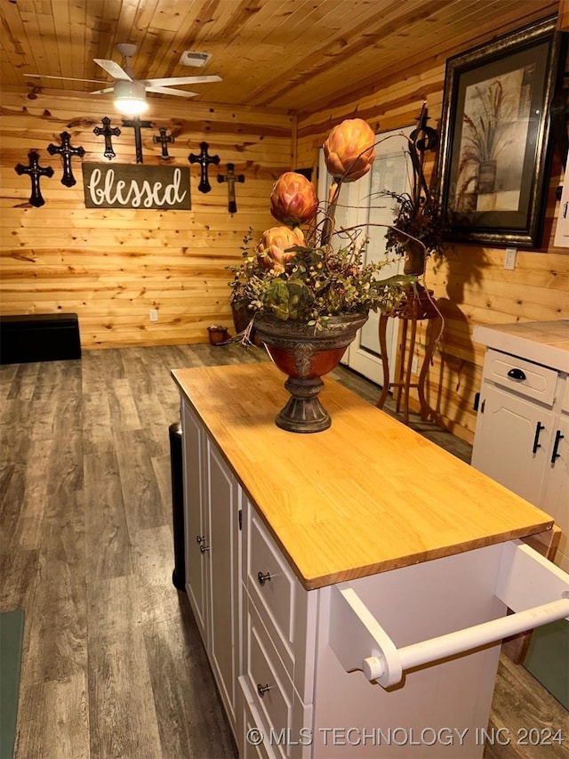 unfurnished dining area with ceiling fan, wood ceiling, dark wood-type flooring, and wooden walls