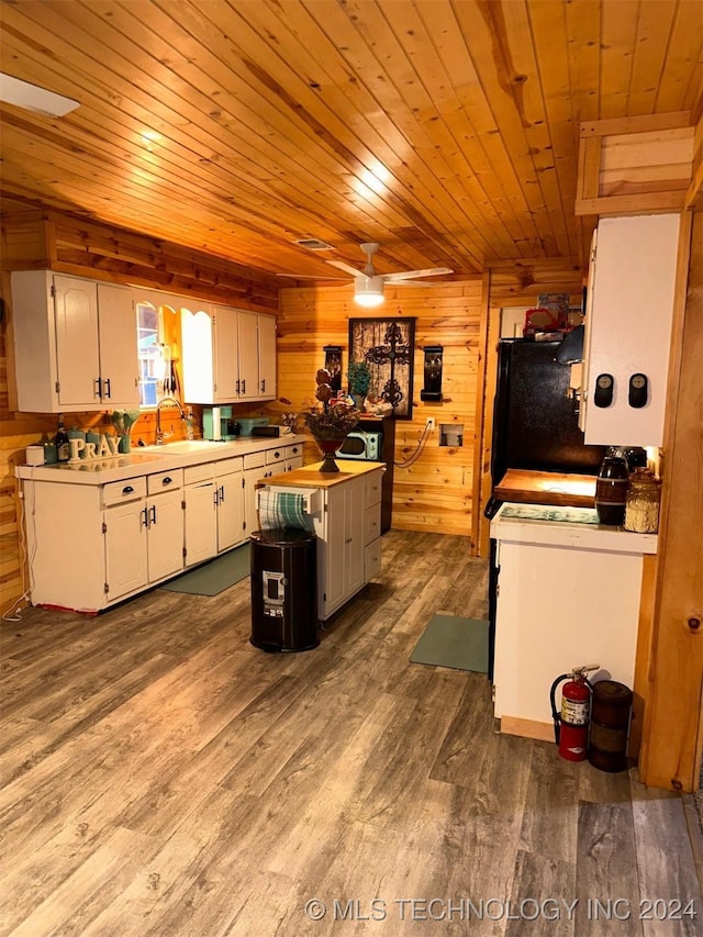 kitchen featuring sink, wooden walls, hardwood / wood-style flooring, a kitchen island, and white cabinetry