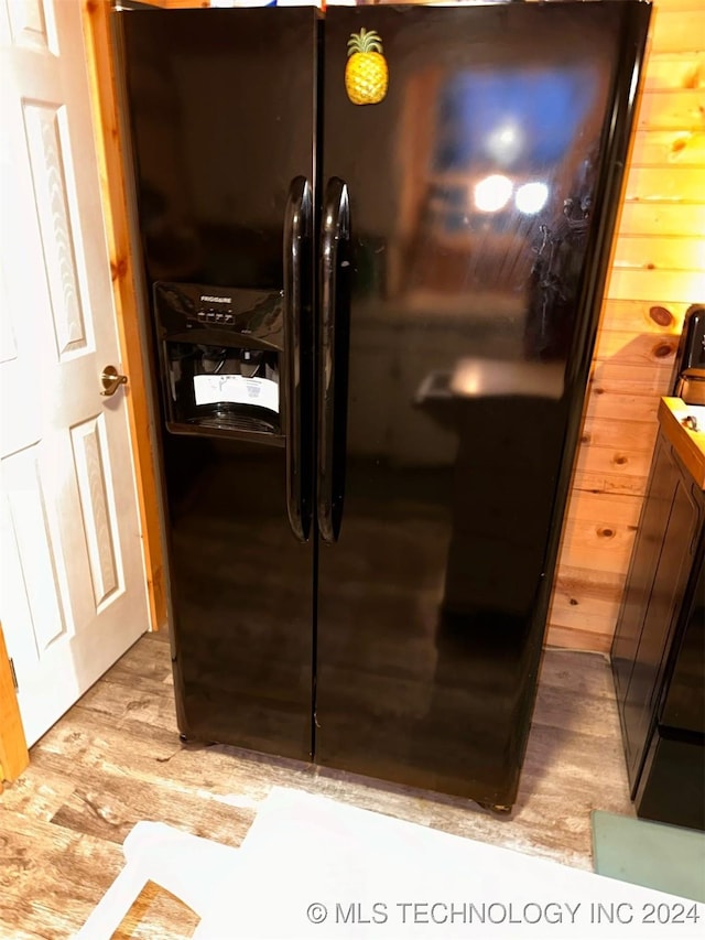 interior details with light wood-type flooring, black fridge, and wood walls