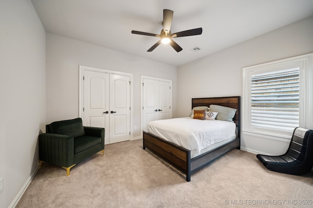 bedroom with two closets, ceiling fan, and light colored carpet