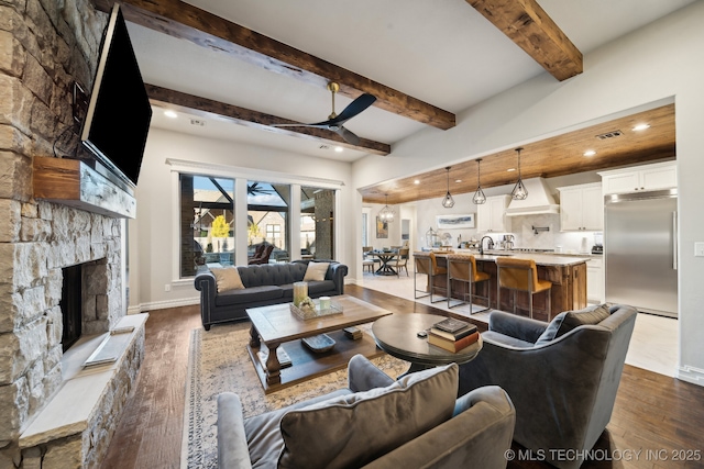 living room featuring sink, a fireplace, beamed ceiling, ceiling fan, and dark wood-type flooring