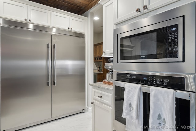 kitchen featuring white cabinetry, wooden ceiling, built in appliances, and light stone counters