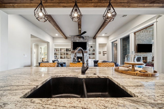 kitchen with sink, hanging light fixtures, a stone fireplace, and built in shelves